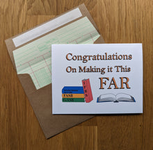 Load image into Gallery viewer, Accounting greeting card, with an image of a book titled "IFRS" leaning against images of 3 stacked books titled "GASB", "FASB", and Securities Exchange Act of 1934", and an open book sitting to the right, with text on top that reads "Congratulations on Making it This FAR", atop an envelope lined in ledger paper