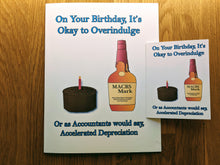 Load image into Gallery viewer, Accounting greeting card, with a birthday cake and a bottle labeled MACRS Mark that parodies a bottle of Makers Mark.  A large jumbo-sized card with this design is in the background, with a smaller-sized card with the same design laid atop the middle right section of the card to show the scale and size of the cards.