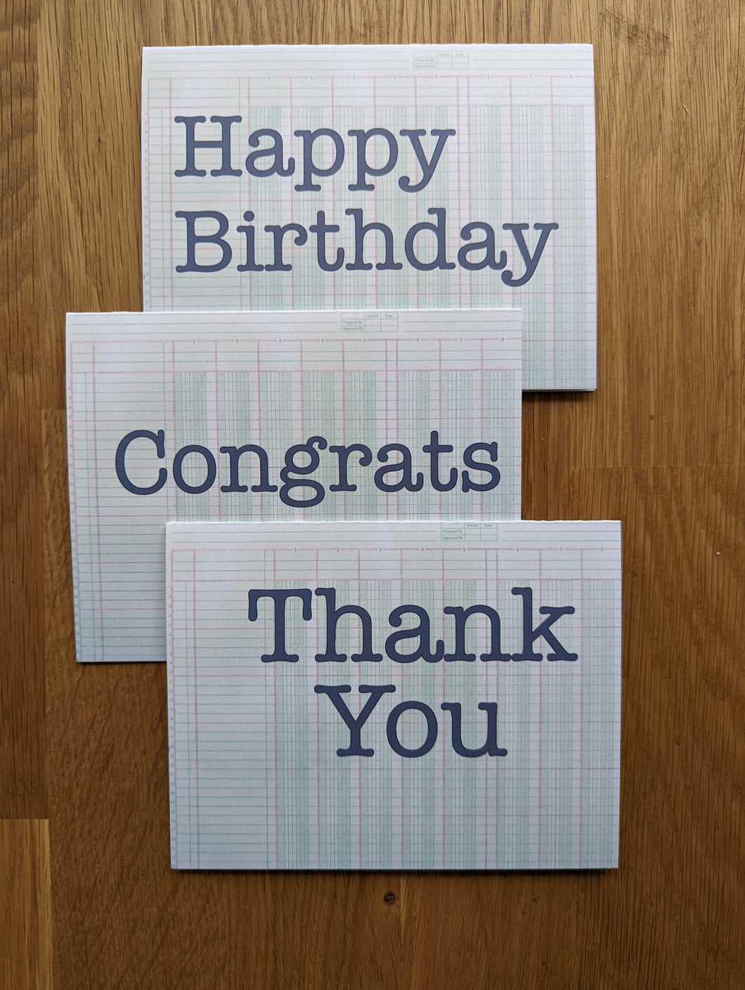 Three accounting greeting cards atop a wooden table that read Happy Birthday, Congrats, and Thank You
